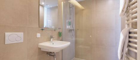 A modern bathroom with a glass-enclosed shower, a white sink, and a towel rack.