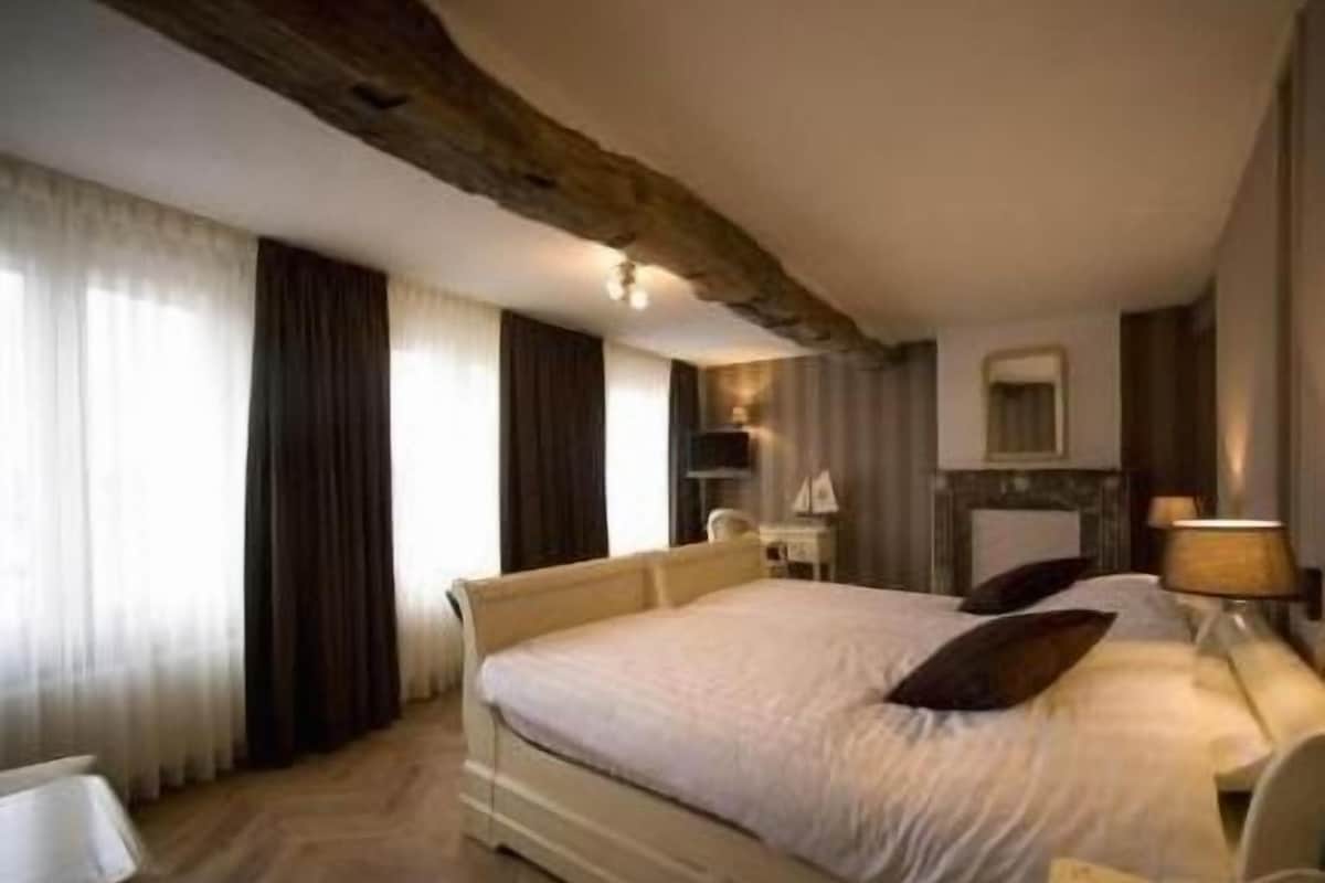 Una habitación de hotel con una cama grande, mesitas de noche, un espejo y una chimenea.