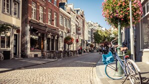 Una calle adoquinada bordeada de edificios históricos, con mesas al aire libre y una bicicleta con cesto.