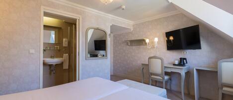 A hotel room with a bed, a desk, a chair, a TV, a mirror, and a bathroom with a sink and towel.