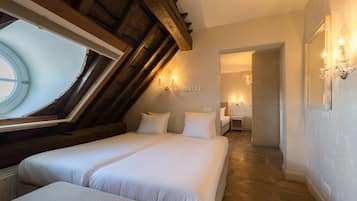 A bedroom with two beds, a skylight, wooden beams, a chandelier, and a hallway leading to another room.