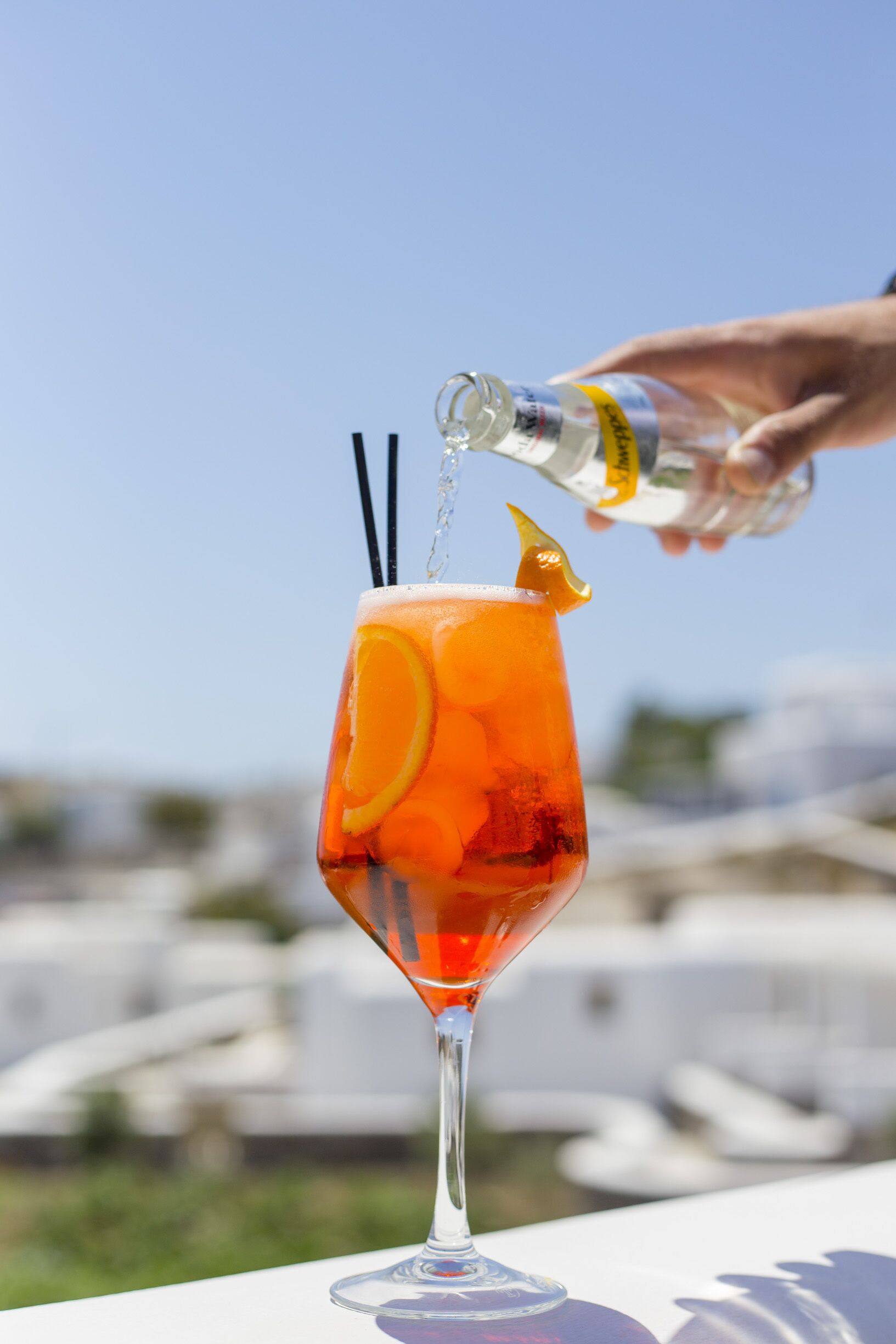 A cocktail in a tall glass with orange slices and a lemon wedge, being poured from a bottle.