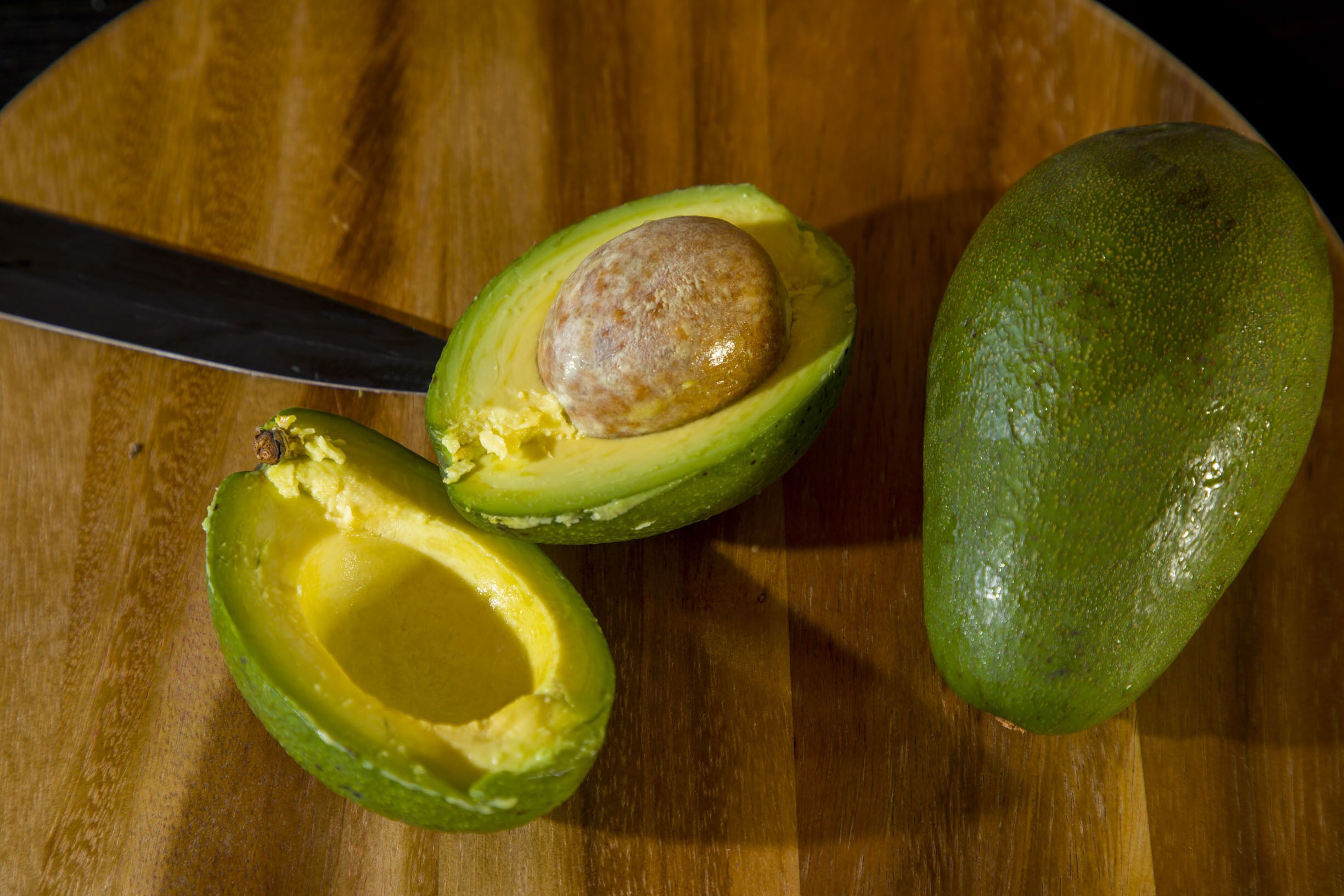 A halved avocado on a wooden cutting board.