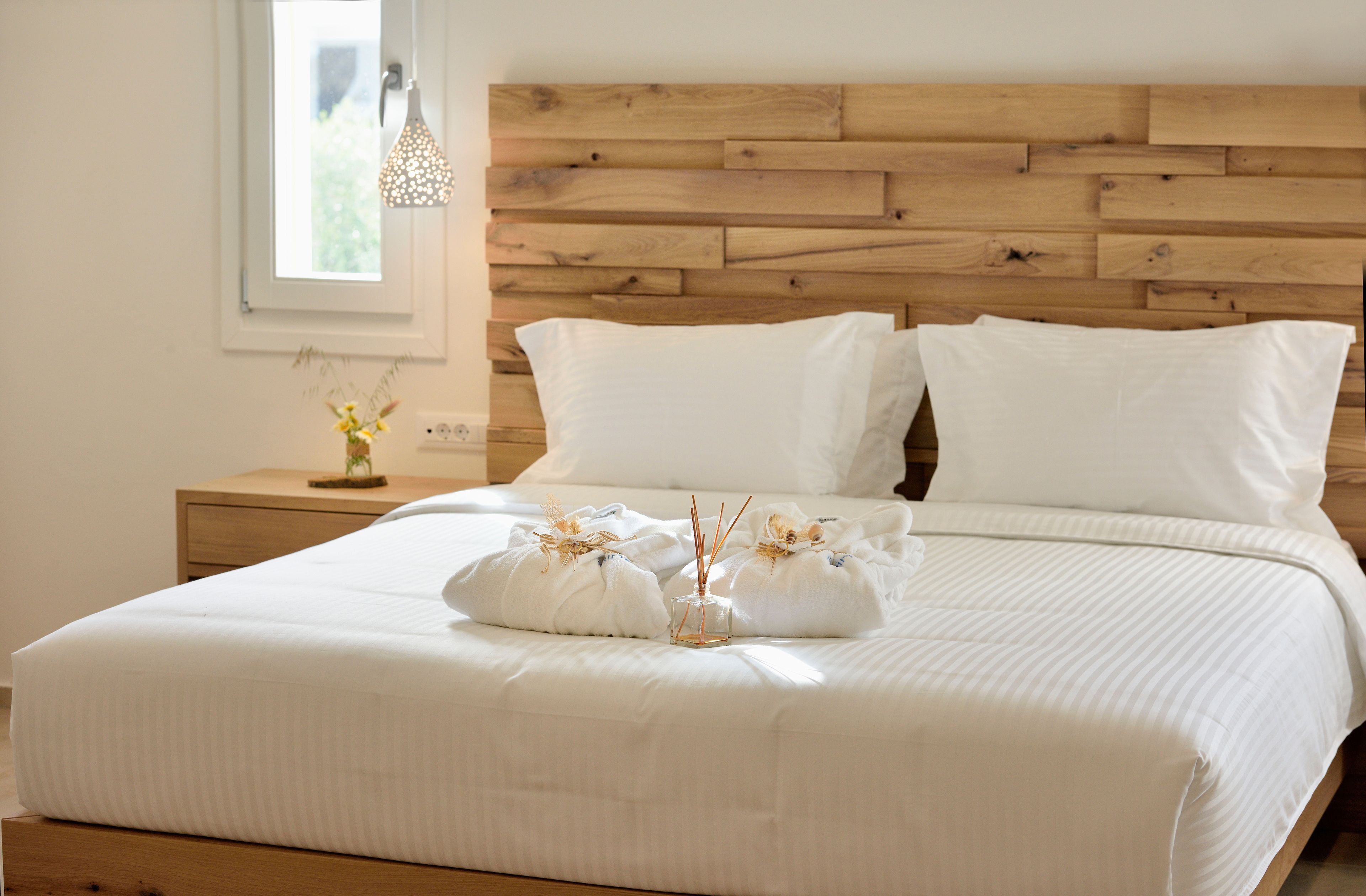 A neatly made bed with white linens, a wooden headboard, and a bedside table with a vase of flowers.