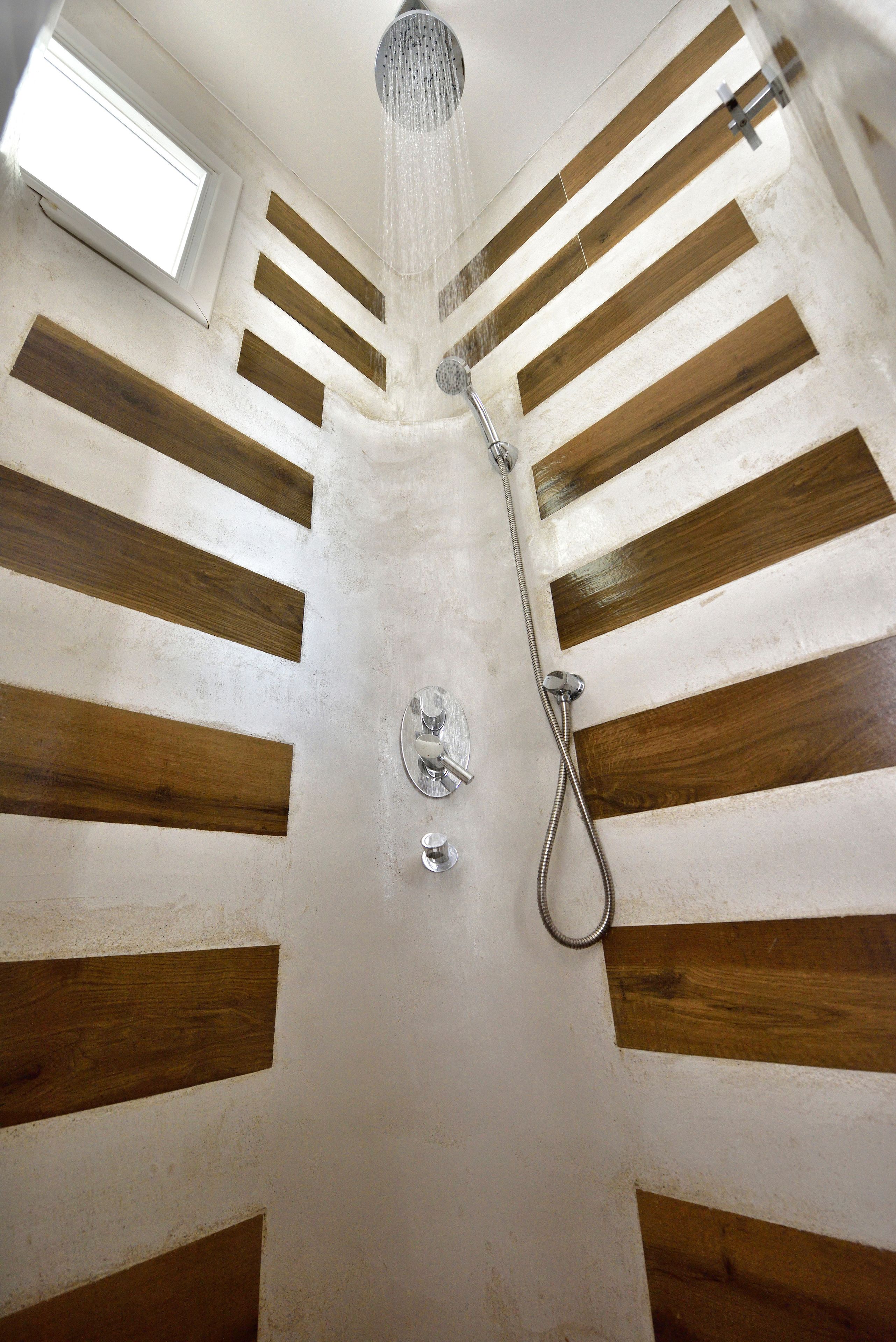 A shower with a rain showerhead and a handheld showerhead, wooden paneling on the walls, and a skylight above.