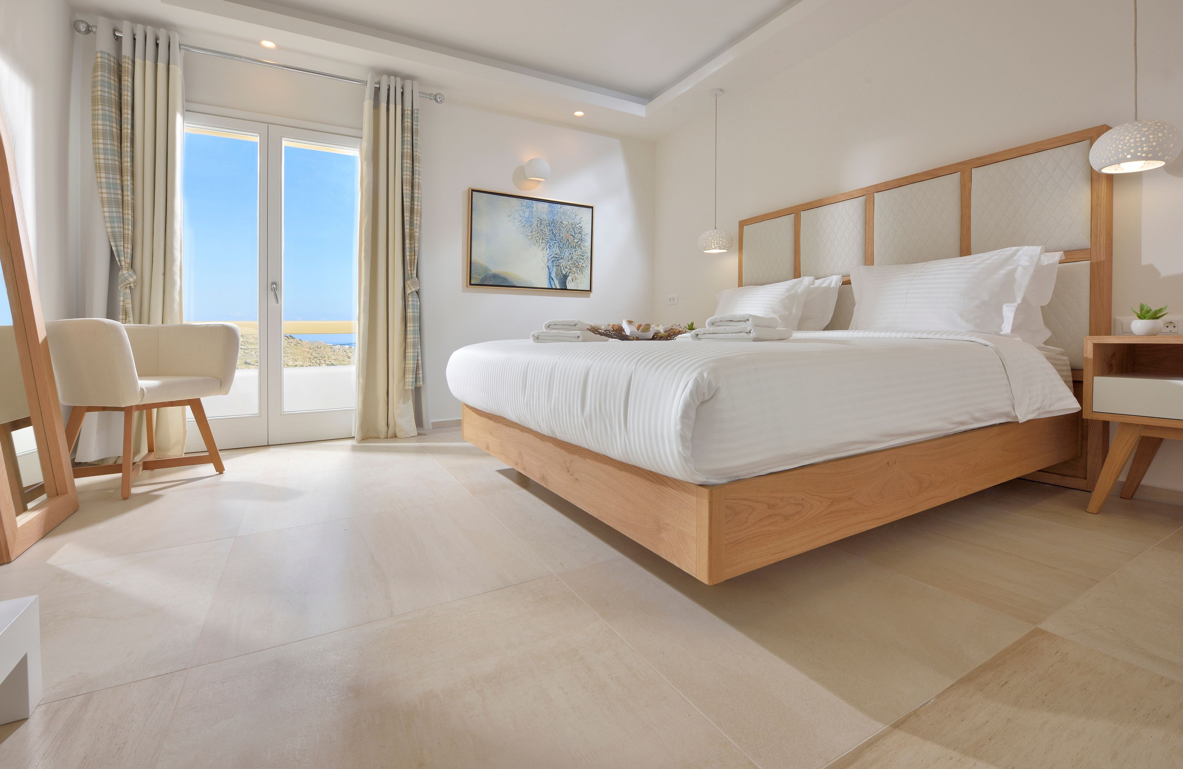 Un dormitorio moderno con una cama grande, una silla y vista al mar a través de puertas de cristal.