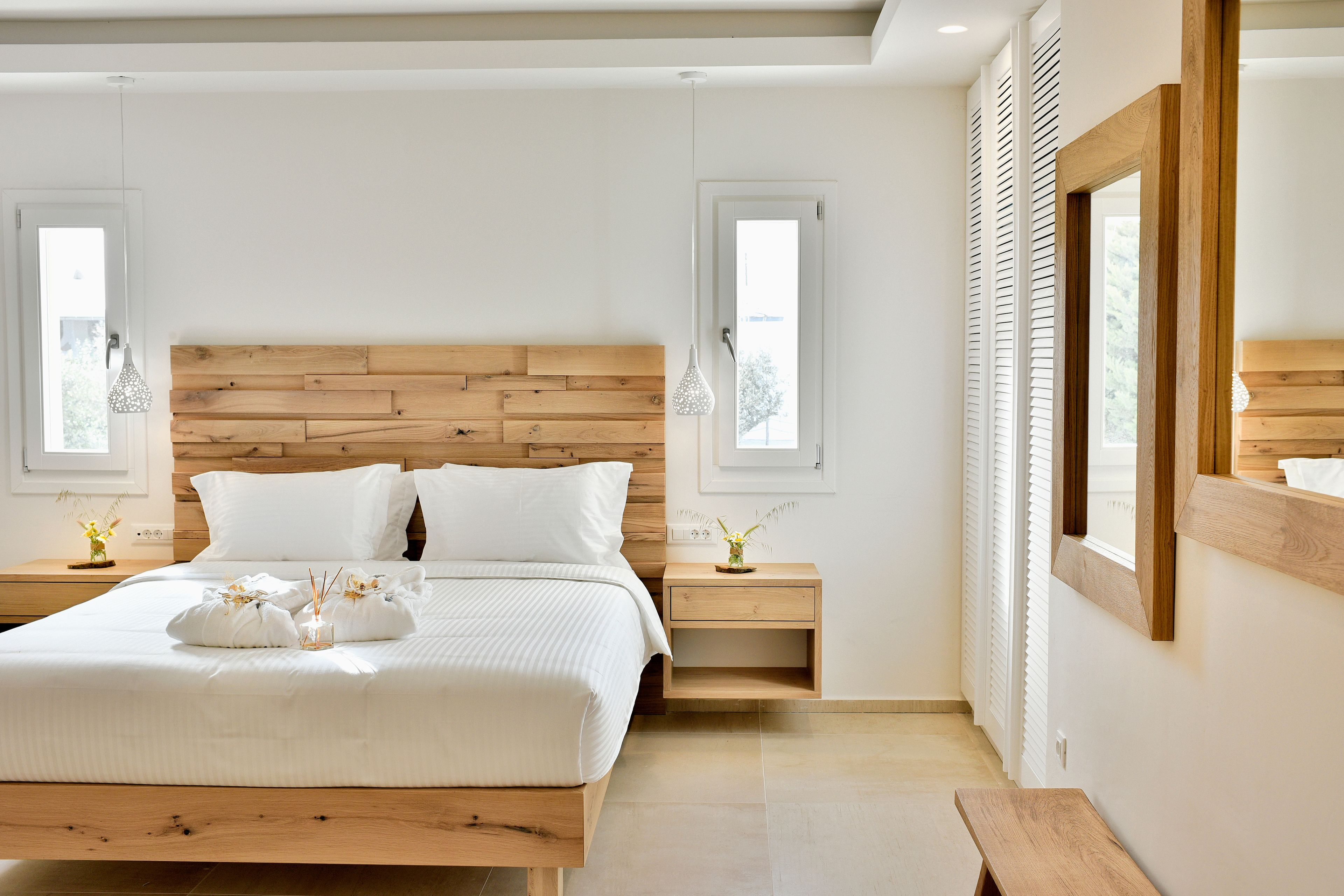 A modern bedroom with a wooden headboard, a large bed with white bedding, two bedside tables with lamps, and a wooden bench.