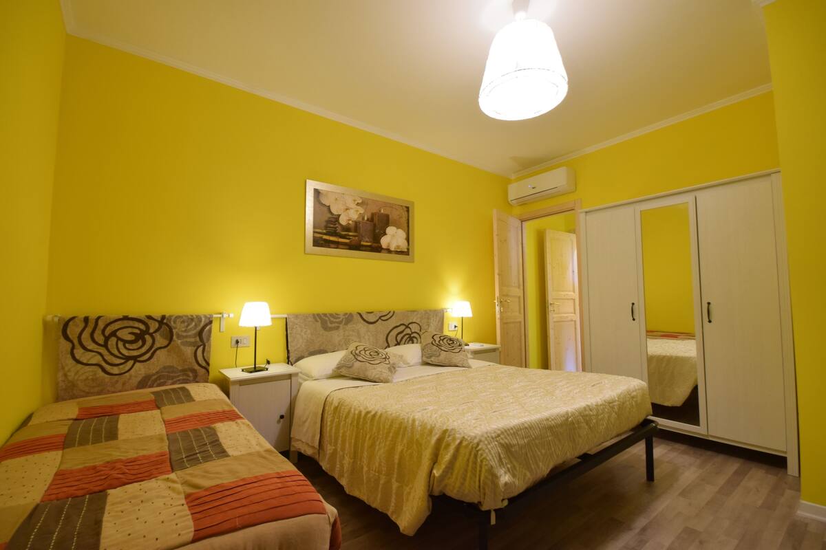 A bedroom with two beds, a nightstand with lamps, a mirror, and a wardrobe.