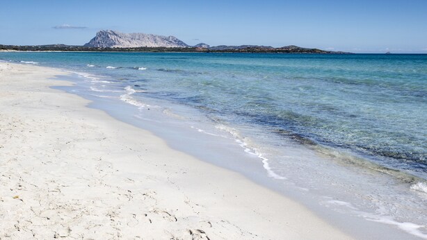 Uma praia com águas turquesa cristalinas e uma montanha ao fundo.