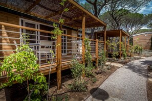A wooden cabin with a covered porch, a dining area with a table and chairs, and a small garden area with various plants. - Camping Internazionale Etruria (Castiglione della Pescaia)