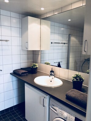 A modern bathroom with a white sink, a mirror, a towel rack, and a shower.
