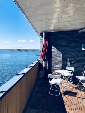 A balcony with a view of the water, a brick wall, and white chairs.