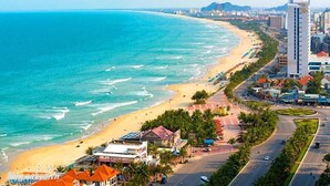 A coastal cityscape with a beach, a road lined with palm trees, and a tall hotel building. - Sepon Blue Hotel (Da Nang)