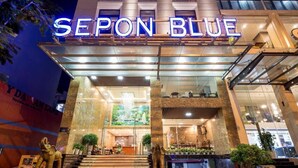 The exterior of the Sepon Blue hotel with a prominent neon sign, a grand entrance with steps, and a reception area visible through the glass facade. - Sepon Blue Hotel (Da Nang)