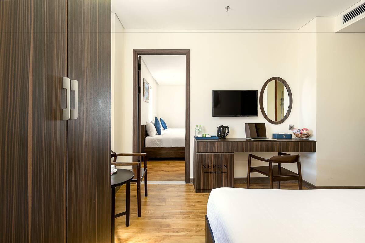 A hotel room with a bed, a desk with a computer, a TV, and a mirror.