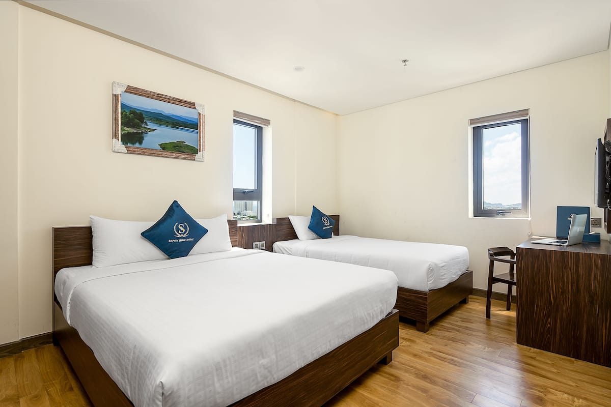 A hotel room with two beds, a desk, and a large window.