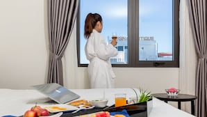 Ein Hotelzimmer mit Bett, Frühstückswagen, Laptop und Blick auf ein Gebäude mit der Aufschrift "REGINA".