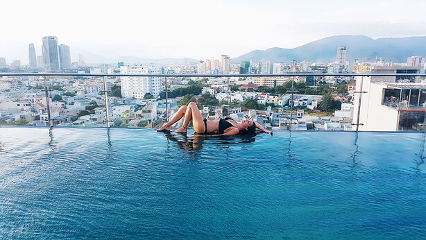 A person relaxing in a rooftop infinity pool with a cityscape view. - Sepon Blue Hotel (Da Nang)