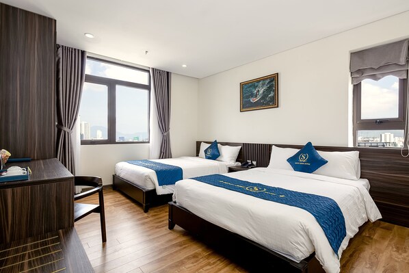 A hotel room with two beds, a desk, and a view of the city. - Sepon Blue Hotel (Da Nang)