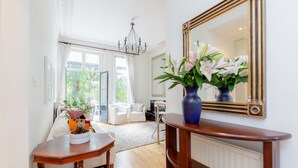 A bright living room with a wooden dining table, white sofas, a large mirror, and a vase of flowers. - Philbeach Balcony- 2bed flat in Earls Ct (London)