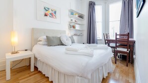 A neatly arranged bedroom with a bed, bedside table, shelves, and a desk. - Philbeach Balcony- 2bed flat in Earls Ct (London)