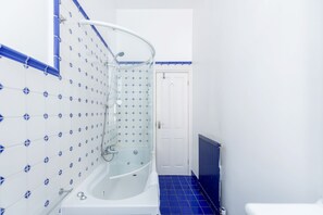 Ein Badezimmer mit einer gläsernen Duschkabine, weißen Fliesen mit blauen Mustern, einer weißen Tür und einem blau gefliesten Boden.