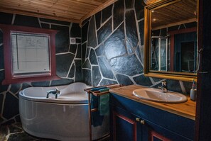 A bathroom with a stone wall, a bathtub, a sink, and a mirror.
