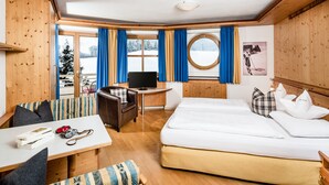 Quarto de hotel com uma cama, uma escrivaninha com cadeira, televisão e vista para uma paisagem nevada.