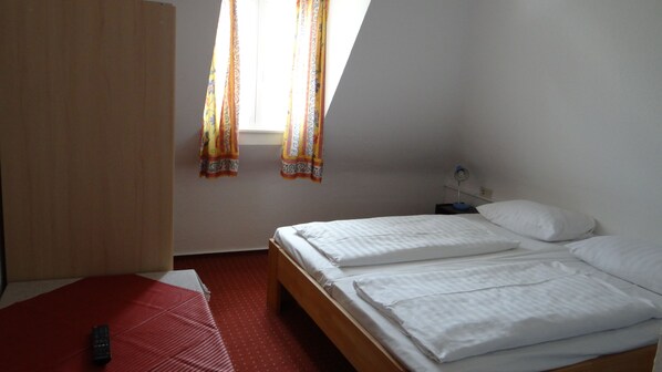 A single-bed room with a wooden wardrobe, a small bedside table with a lamp, and a window with curtains. - Hotel Meesenburg (Würzburg)