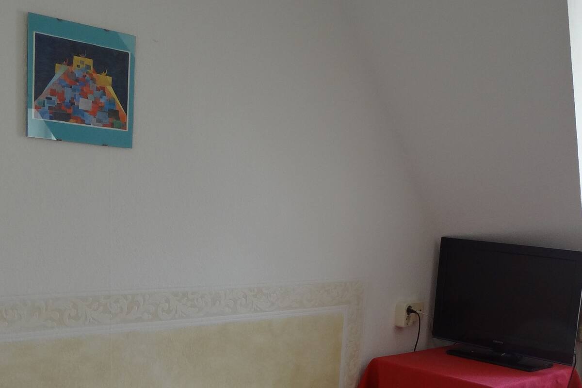 A single bed with white bedding, a television on a red table, and a framed picture on the wall.
