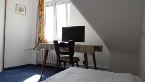 A room with a bed, a desk with a computer, a chair, a radiator, and a window with curtains. - Hotel Meesenburg (Würzburg)