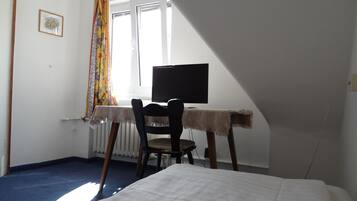 Ein Zimmer mit einem Bett, einem Schreibtisch mit Computer, einem Stuhl, einem Heizkörper und einem Fenster mit Vorhängen.