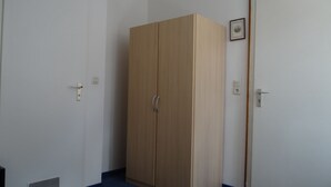 A room with a wooden wardrobe, a door with a handle, and a light switch on the wall. - Hotel Meesenburg (Würzburg)