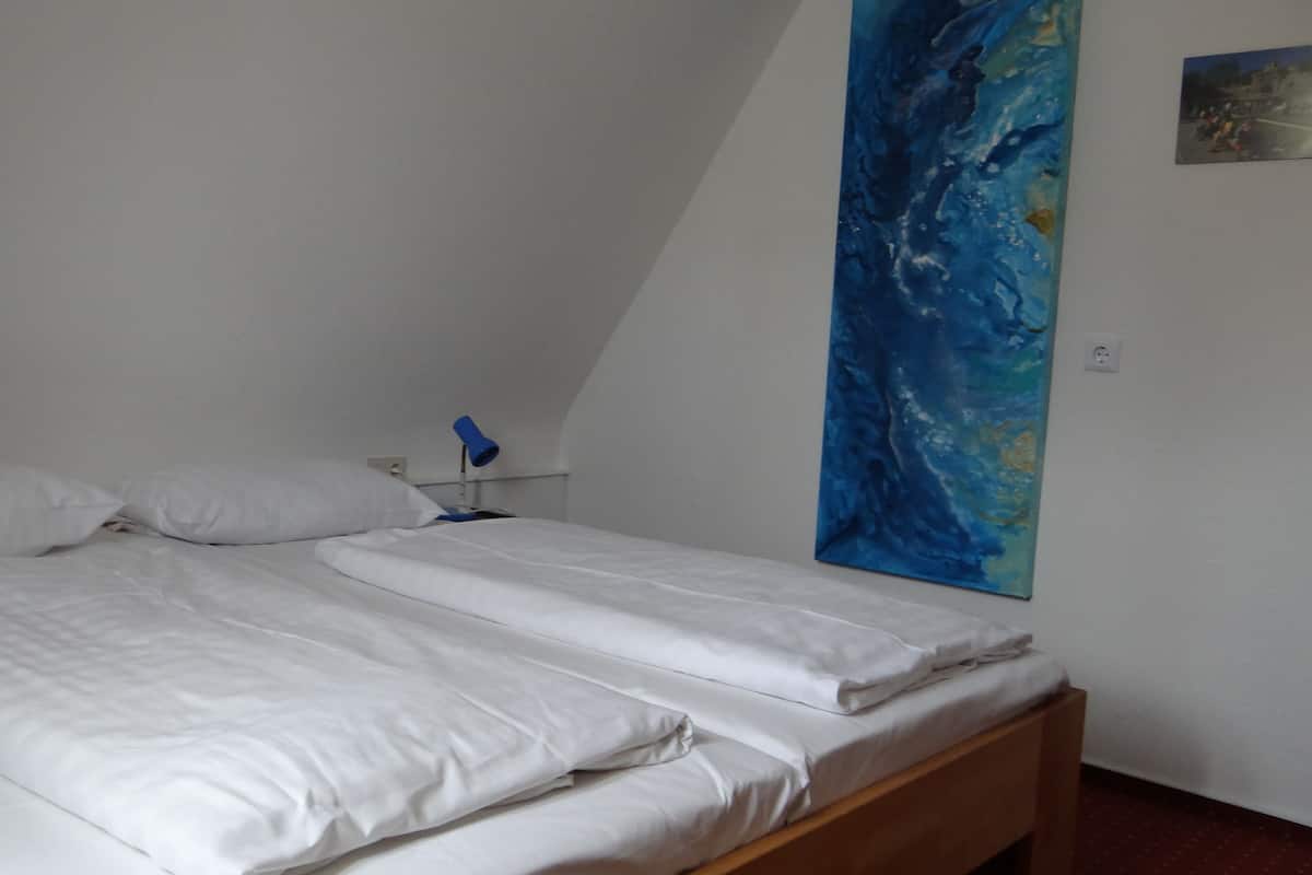 A bed with white linens, a blue lamp on a bedside table, and a large abstract painting on the wall.