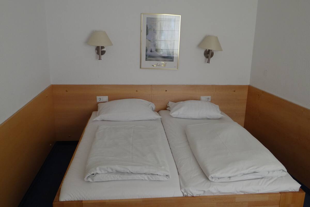 A double bed with white linens, two wall-mounted lamps, and a framed picture above the bed.