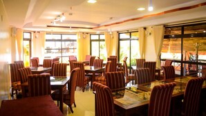 A restaurant with multiple tables and chairs, large windows with curtains, and a ceiling with recessed lighting. - Regency Mount Kenya Hotel (Ethi)