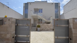 A modern building with a staircase leading to an upper floor. There are two gates with a potted plant in front. - White (Porto Cesareo)