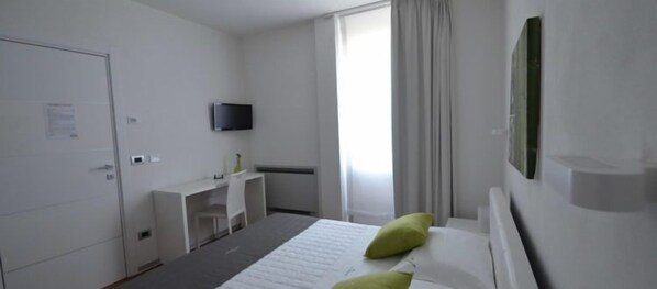 Habitación de hotel con cama, escritorio, silla, televisor de pantalla plana y ventana con cortinas.