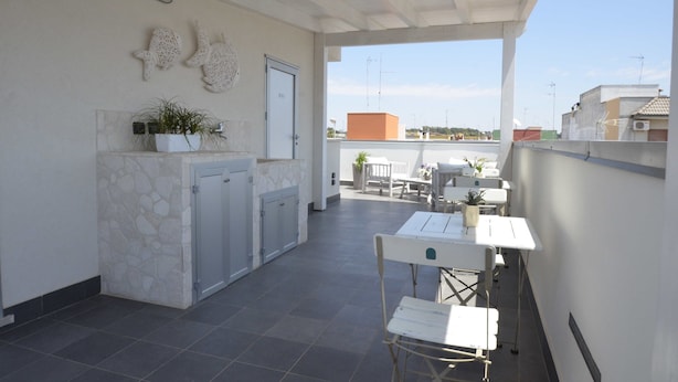 A covered outdoor area with a dining table and chairs, a potted plant, and a stone wall. - White (Porto Cesareo)