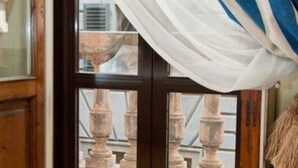 A room with a wooden door, a view of a balcony with stone balustrades, and a window with a view of the outside. - Residenza dei Pucci (Florence)