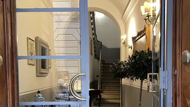 A hallway with a checkered floor, a staircase, and a door leading to a room with a mirror and a vase. - Residenza dei Pucci (Florence)