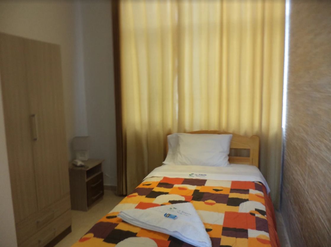 Een hotelkamer met een bed, een houten kast, een klein nachtkastje en een gordijn.