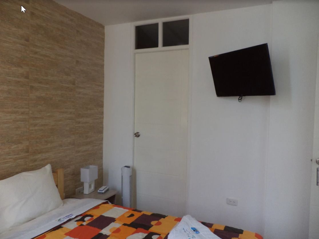 Un dormitorio con una cama, una puerta blanca, un televisor montado en la pared y un revestimiento de pared de madera con textura.