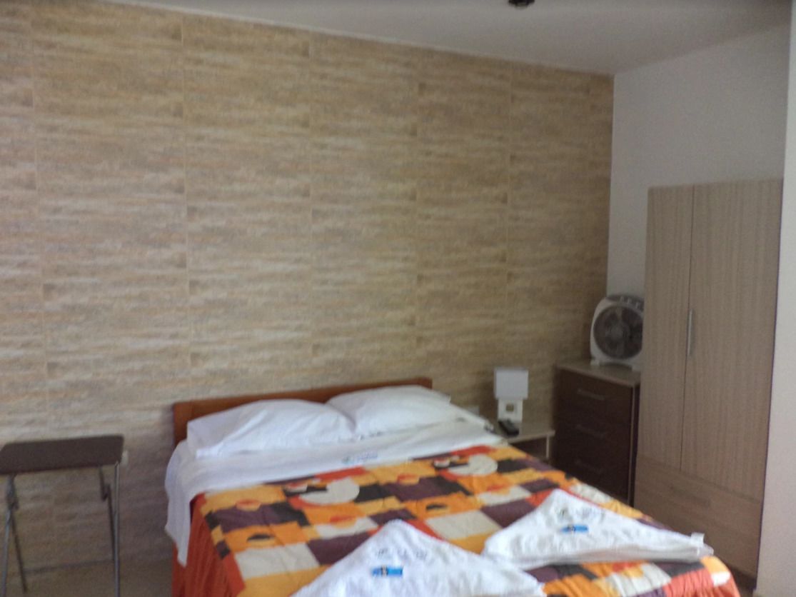 Ett sovrum med en vägg som har ett mönster av tegelstenar, en säng med ett täcke, ett sängbord med en lampa och en garderob.