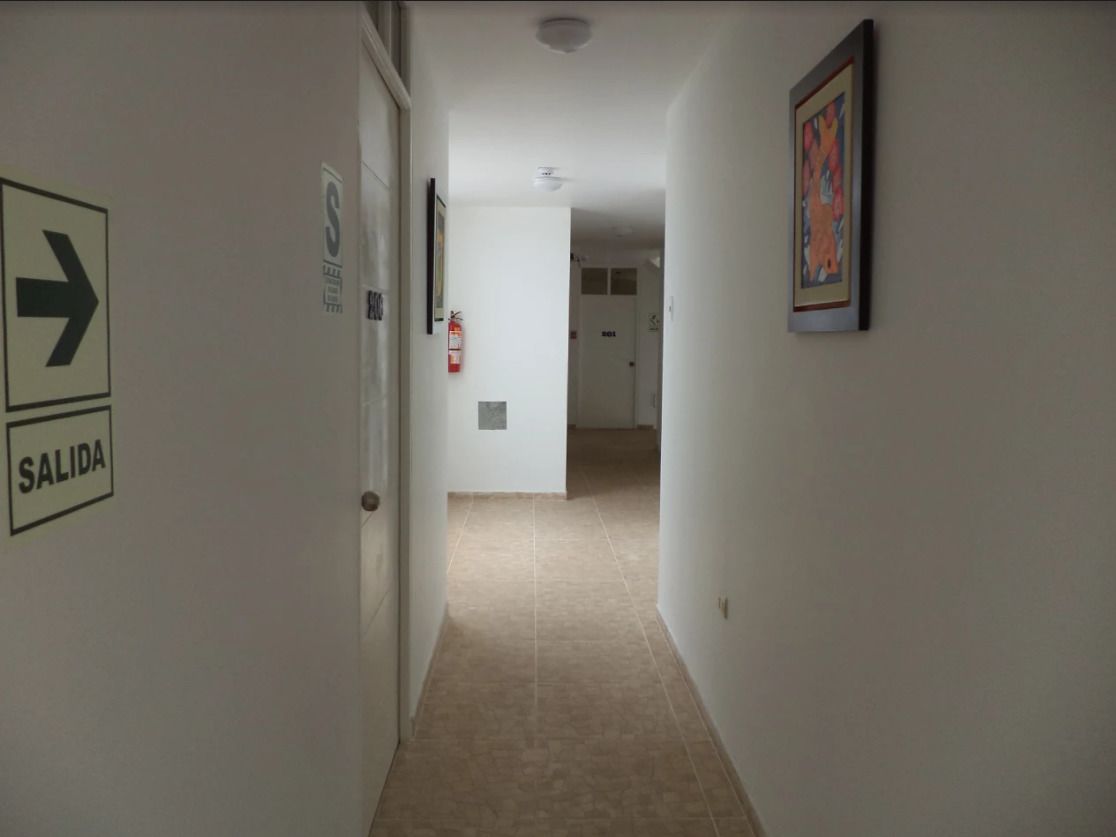 A hallway with a 'SALIDA' sign, a directional arrow, and a framed picture on the wall.