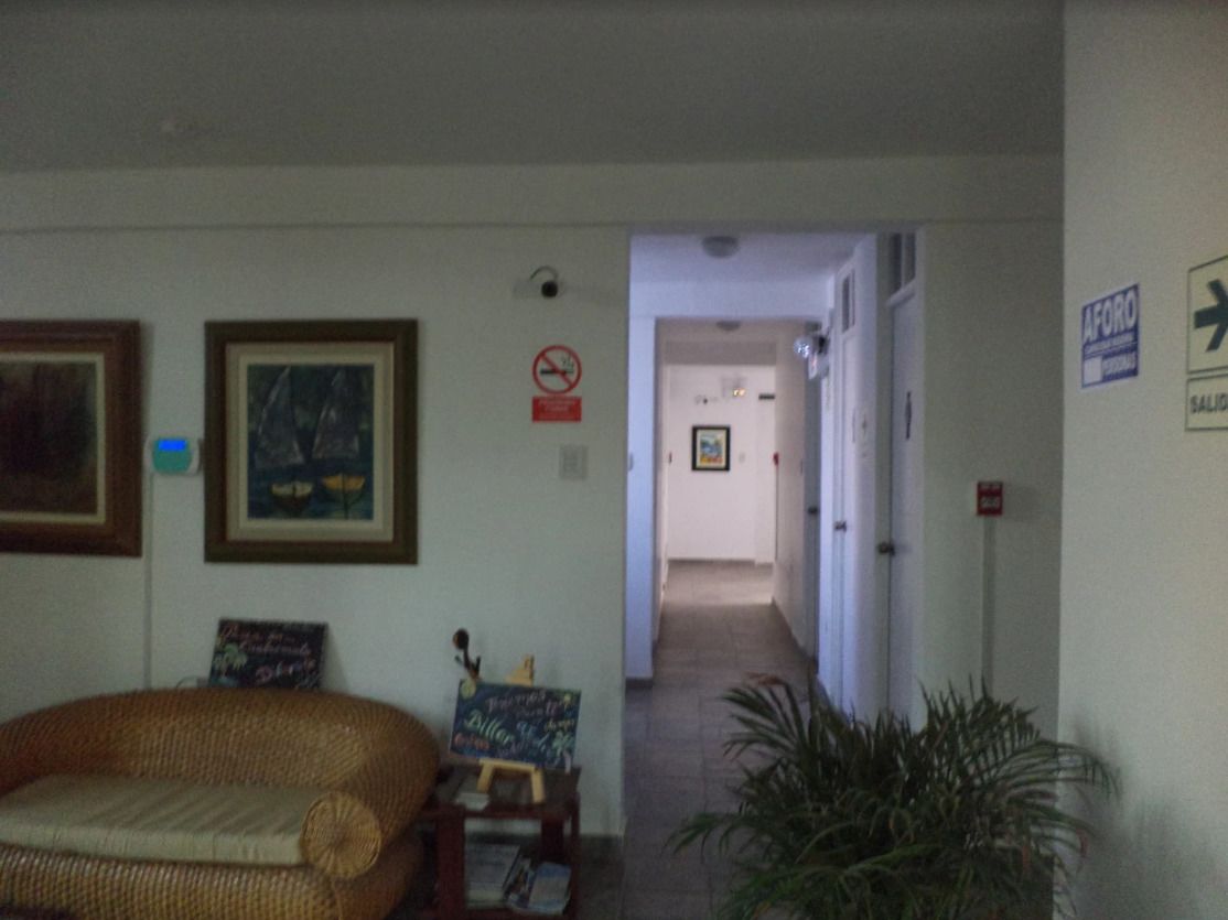Un couloir avec un canapé en osier, des œuvres d’art encadrées et un tableau noir sur lequel on a écrit.