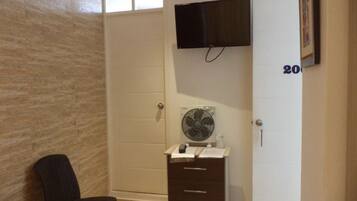 Una habitación con cama, una silla, cómoda, televisor montado en la pared y una puerta con un número.