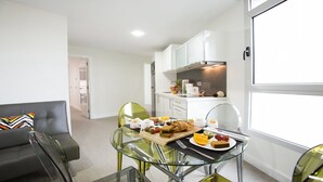 A modern living room with a glass dining table set for breakfast, a grey sofa, and a kitchen in the background. - Valentina Beach (Las Palmas de Gran Canaria)