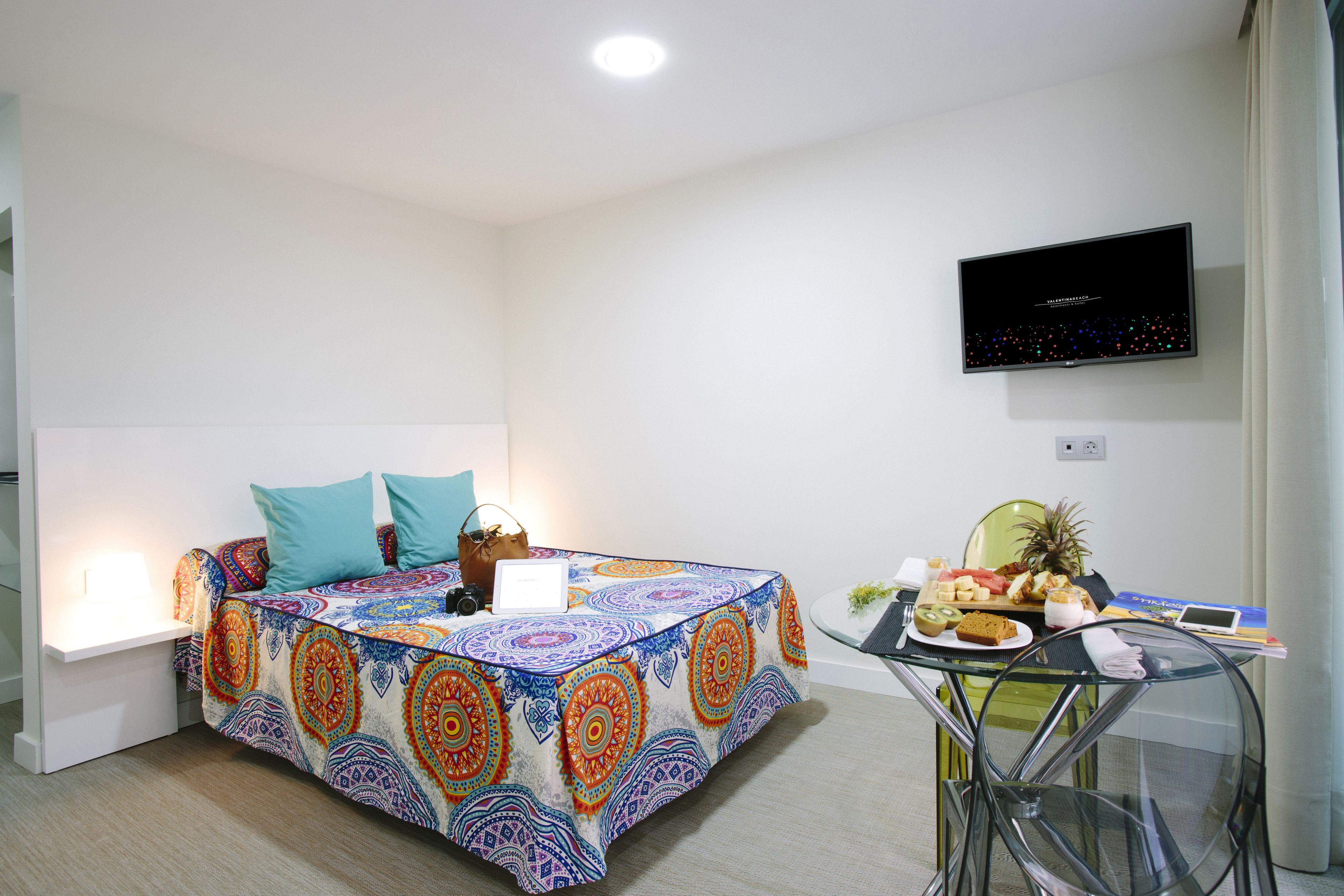 Una habitación con una cama, una mesa con comida, una computadora portátil y un televisor en la pared.