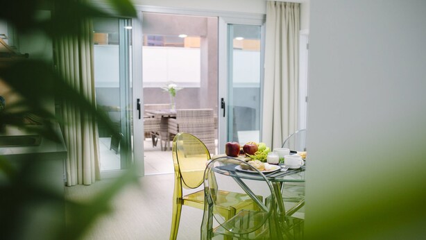A modern dining area with a glass table and chairs, a breakfast setting with fruits and beverages, and a view of an outdoor patio with a dining table and chairs. - Valentina Beach (Las Palmas de Gran Canaria)